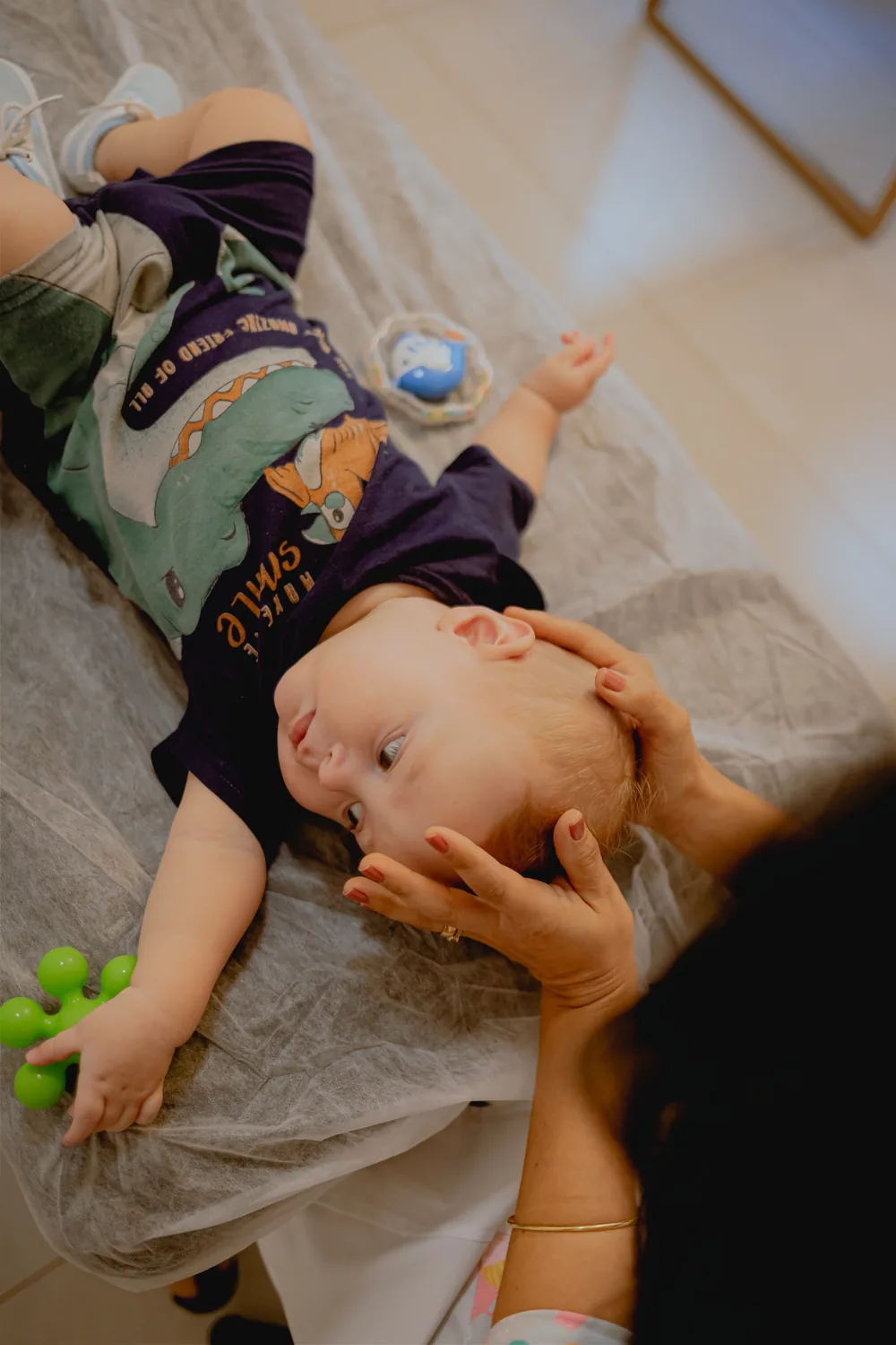 Mãos da Dra. Ligiane Gama aplicando técnica craniana suave em um bebê durante sessão de osteopatia pediátrica